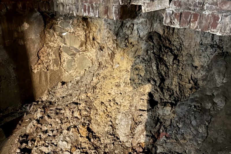 Structural foundation repair showing exposed soil, excavated stone wall, and brick support restoration