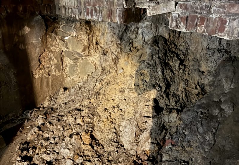 Structural foundation repair showing exposed soil, excavated stone wall, and brick support restoration