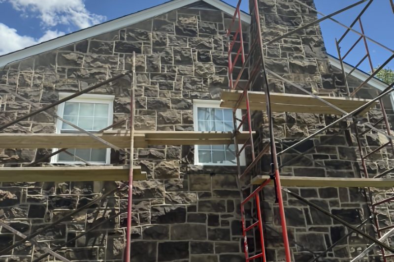 Scaffolding set up against a multi-story stone home for chimney restoration and exterior masonry repointing