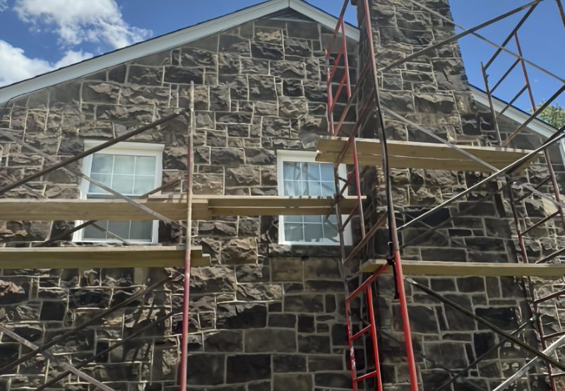 Scaffolding set up against a multi-story stone home for chimney restoration and exterior masonry repointing